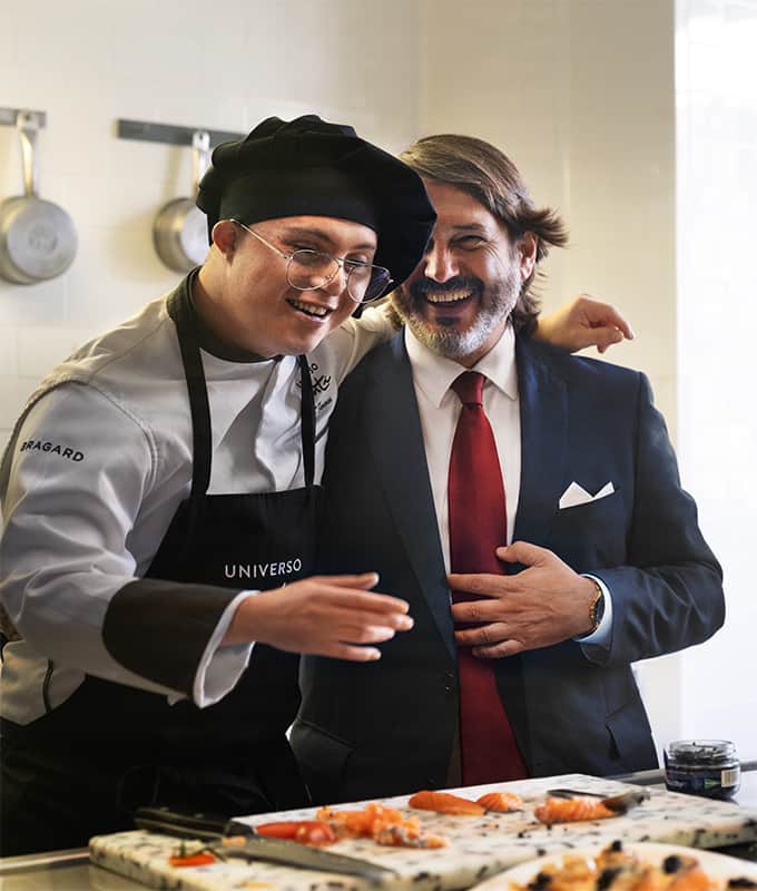 En kok med handicap griner ved siden af ​​en mand i jakkesæt i køkkenet