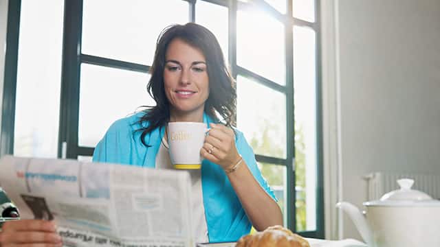 kvinde drikker en kop kaffe, mens hun læser en avis